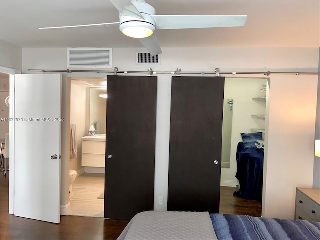 bedroom with ceiling fan, dark wood-type flooring, connected bathroom, a walk in closet, and a closet