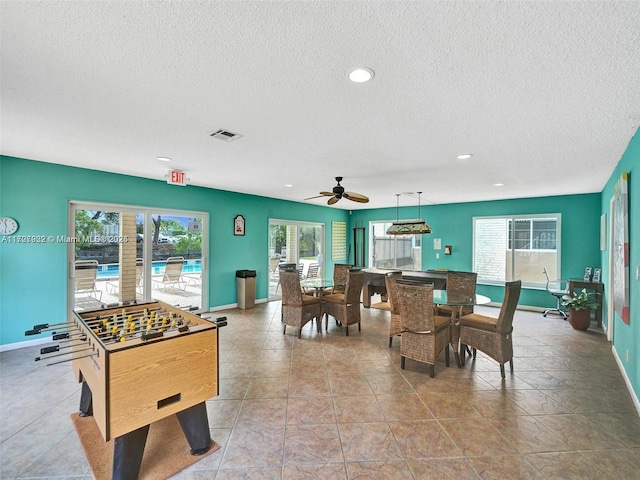 game room with a textured ceiling, light tile patterned floors, and a healthy amount of sunlight