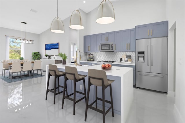 kitchen featuring an island with sink, appliances with stainless steel finishes, decorative backsplash, a kitchen breakfast bar, and pendant lighting