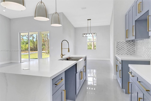 kitchen with tasteful backsplash, a kitchen island with sink, decorative light fixtures, light tile patterned flooring, and sink