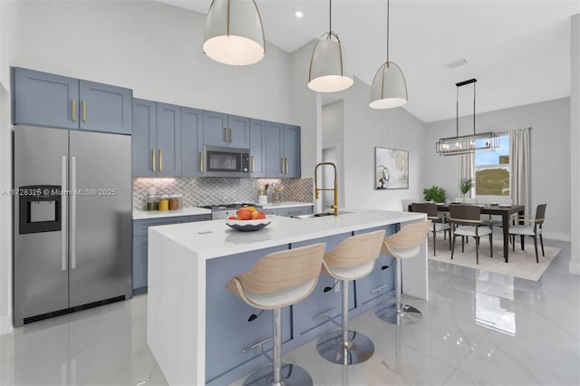 kitchen with an island with sink, appliances with stainless steel finishes, decorative light fixtures, and sink