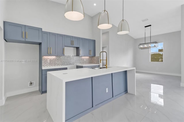 kitchen with hanging light fixtures, sink, a center island with sink, and backsplash