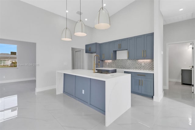 kitchen featuring backsplash, a towering ceiling, an island with sink, and pendant lighting