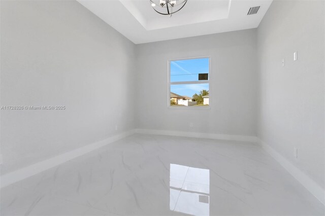 spare room featuring a tray ceiling and a notable chandelier