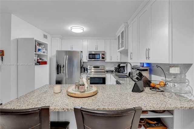 kitchen with appliances with stainless steel finishes, white cabinetry, sink, a kitchen breakfast bar, and kitchen peninsula