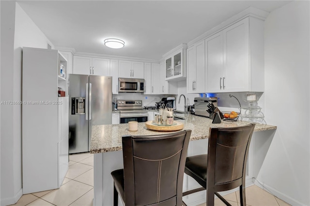 kitchen with white cabinetry, stainless steel appliances, a kitchen breakfast bar, light stone counters, and kitchen peninsula