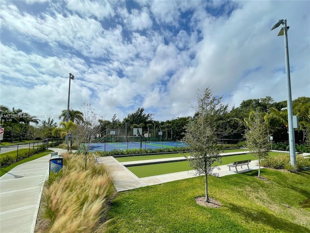 view of community featuring tennis court and a yard