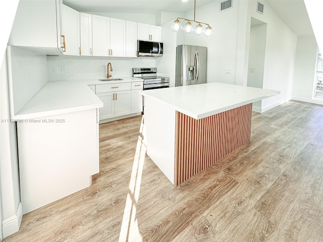 kitchen with white cabinetry, hanging light fixtures, a kitchen island, stainless steel appliances, and lofted ceiling