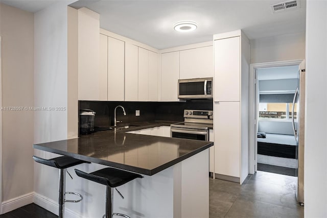 kitchen featuring appliances with stainless steel finishes, white cabinets, sink, a kitchen breakfast bar, and kitchen peninsula