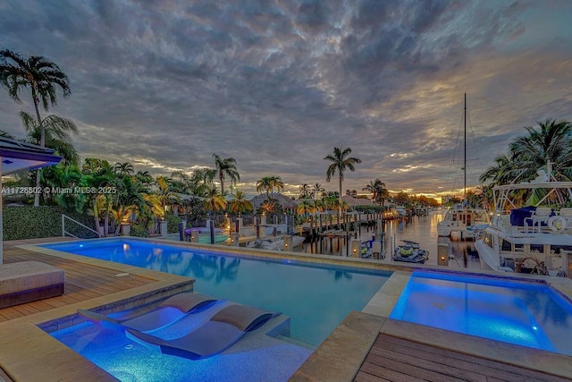 pool at dusk with a water view and an in ground hot tub