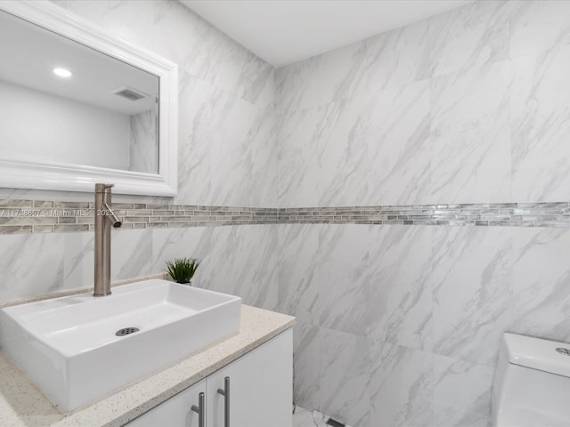 bathroom with toilet, tile walls, and vanity