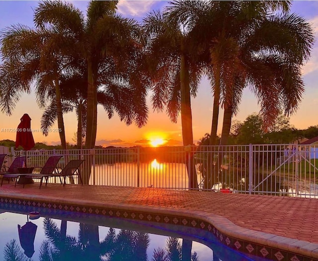 pool at dusk with a water view and a patio