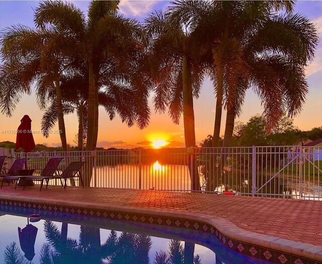 pool at dusk with a patio and a water view