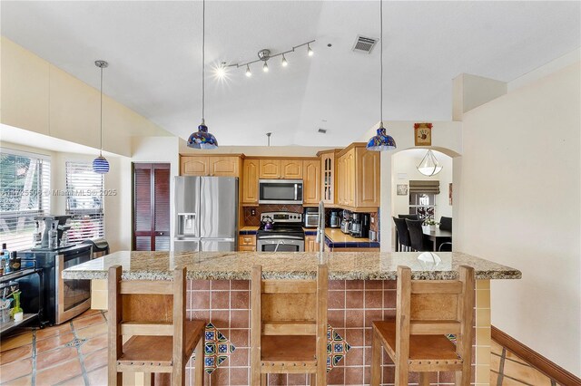 kitchen with vaulted ceiling, appliances with stainless steel finishes, a breakfast bar, pendant lighting, and backsplash