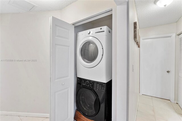 laundry area with stacked washer / dryer, a textured ceiling, and light tile patterned floors