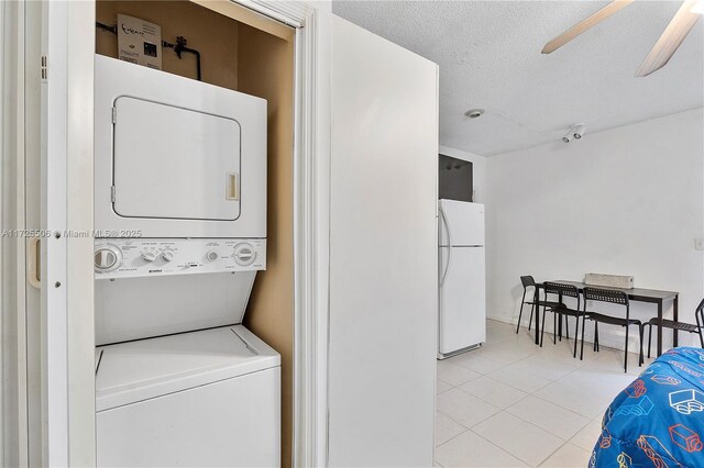 laundry room featuring stacked washer and dryer, ceiling fan, light tile patterned floors, and a textured ceiling