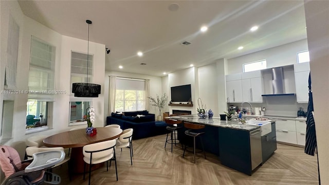 kitchen featuring light parquet floors, an island with sink, wall chimney range hood, and white cabinets