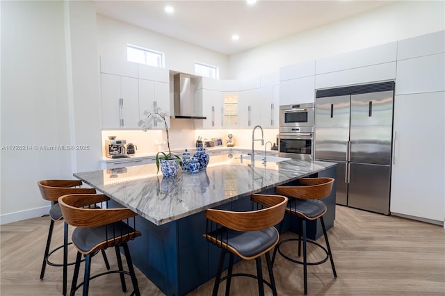 kitchen with light parquet flooring, appliances with stainless steel finishes, wall chimney range hood, and a kitchen bar