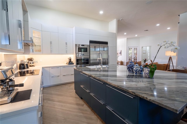 kitchen featuring appliances with stainless steel finishes, dark stone countertops, white cabinets, a center island, and light wood-type flooring