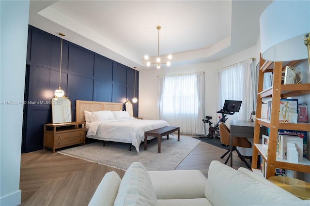 bedroom with light parquet flooring, a notable chandelier, and a tray ceiling