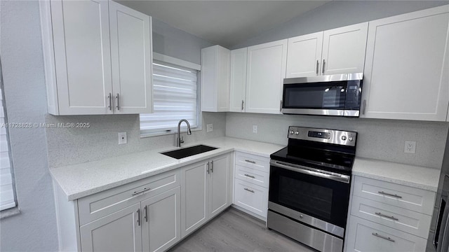 kitchen with vaulted ceiling, white cabinetry, sink, light hardwood / wood-style floors, and stainless steel appliances