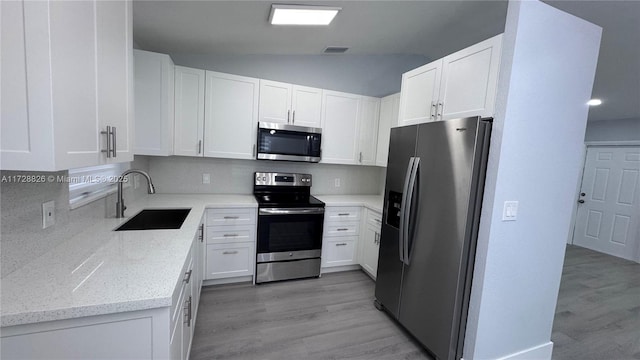 kitchen with sink, white cabinetry, vaulted ceiling, appliances with stainless steel finishes, and light stone countertops