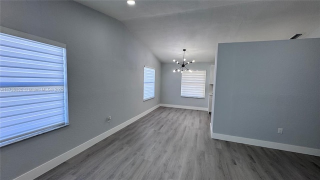 unfurnished room featuring hardwood / wood-style flooring, lofted ceiling, and a chandelier