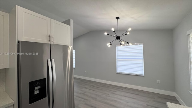 kitchen with stainless steel fridge, white cabinetry, decorative light fixtures, vaulted ceiling, and light wood-type flooring