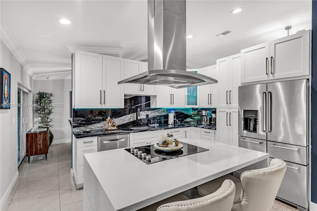 kitchen featuring white cabinets, appliances with stainless steel finishes, island exhaust hood, a kitchen breakfast bar, and ornamental molding