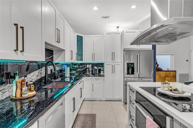 kitchen featuring appliances with stainless steel finishes, white cabinetry, dark stone countertops, sink, and island range hood