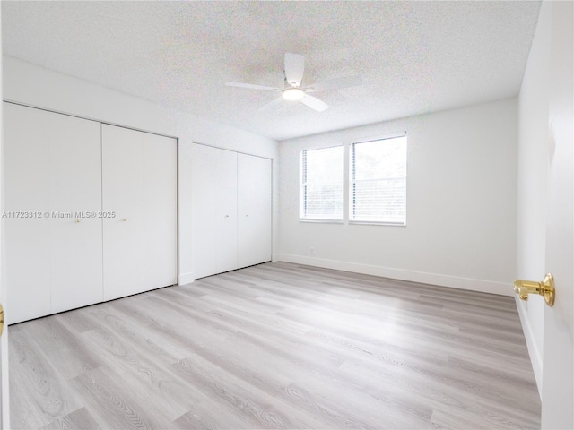 unfurnished bedroom with ceiling fan, two closets, a textured ceiling, and light hardwood / wood-style flooring