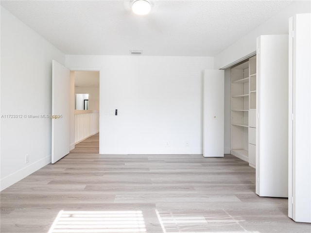 unfurnished bedroom with a textured ceiling, a closet, and light wood-type flooring