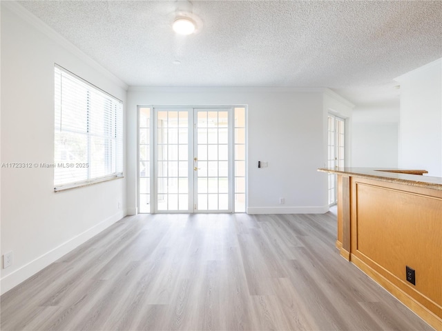 empty room featuring a textured ceiling, crown molding, french doors, and light wood-type flooring