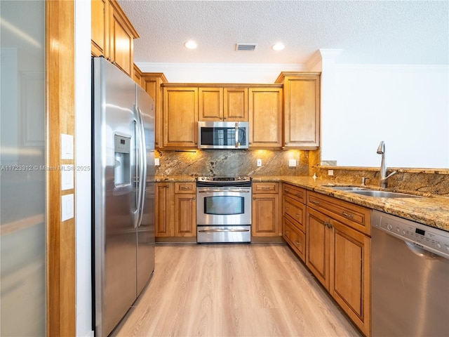 kitchen with light hardwood / wood-style floors, appliances with stainless steel finishes, light stone countertops, a textured ceiling, and sink