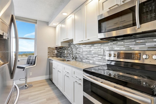 kitchen with white cabinets, appliances with stainless steel finishes, sink, backsplash, and light stone counters