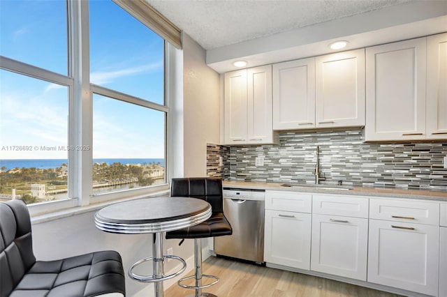 kitchen with stainless steel dishwasher, white cabinets, light stone counters, and sink