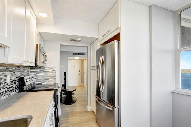 kitchen with appliances with stainless steel finishes, backsplash, white cabinets, a textured ceiling, and light hardwood / wood-style flooring