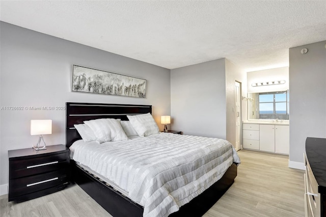 bedroom featuring ensuite bathroom, light wood-type flooring, and a textured ceiling