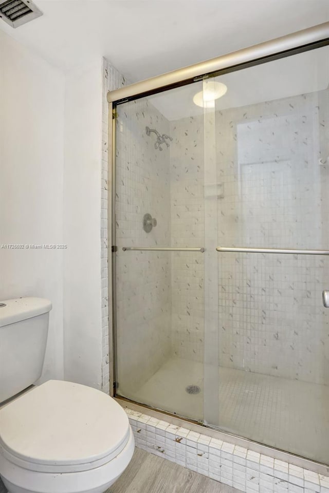 bathroom with hardwood / wood-style floors, an enclosed shower, and toilet