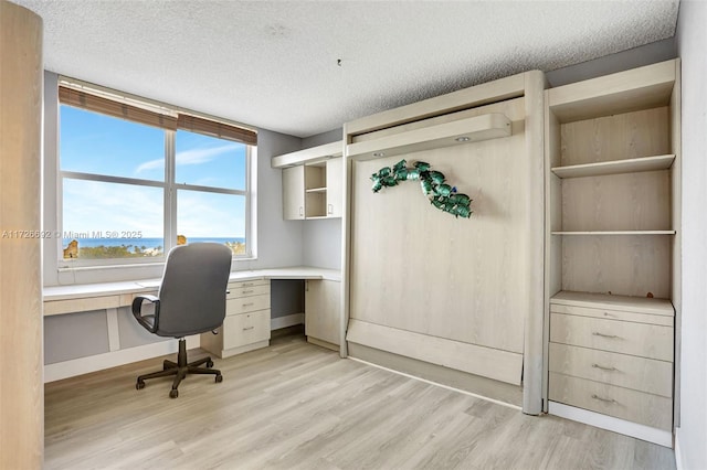 office with a textured ceiling, light hardwood / wood-style flooring, and built in desk