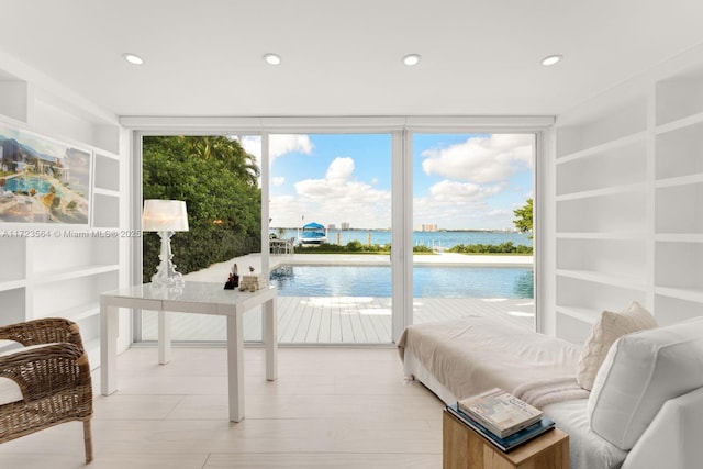 bedroom featuring a water view, access to outside, floor to ceiling windows, and light hardwood / wood-style floors