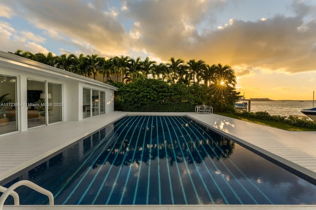 pool at dusk with a water view and a patio