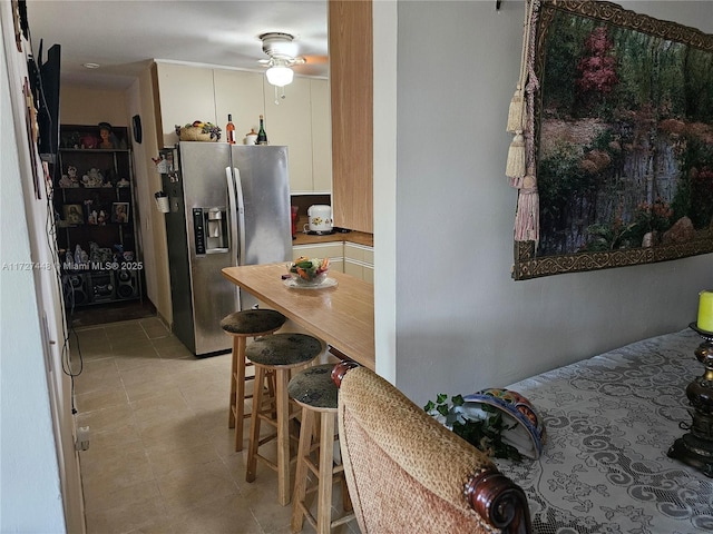 kitchen with stainless steel fridge, white cabinets, a ceiling fan, and light tile patterned flooring