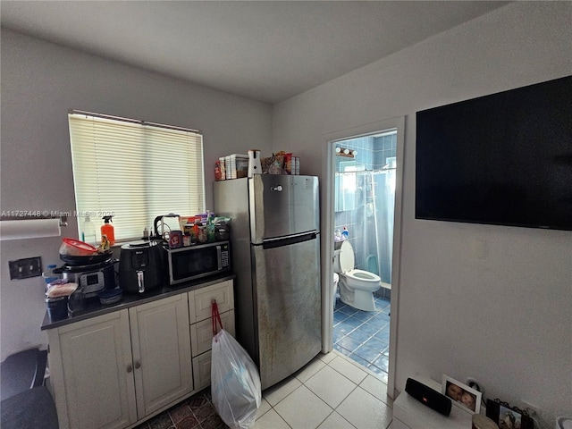 kitchen featuring black microwave, dark countertops, freestanding refrigerator, white cabinetry, and light tile patterned flooring