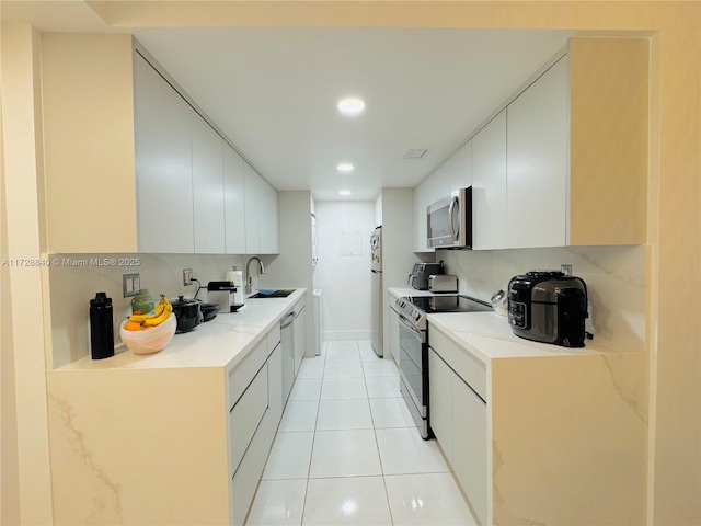 kitchen with light tile patterned floors, appliances with stainless steel finishes, white cabinets, and sink