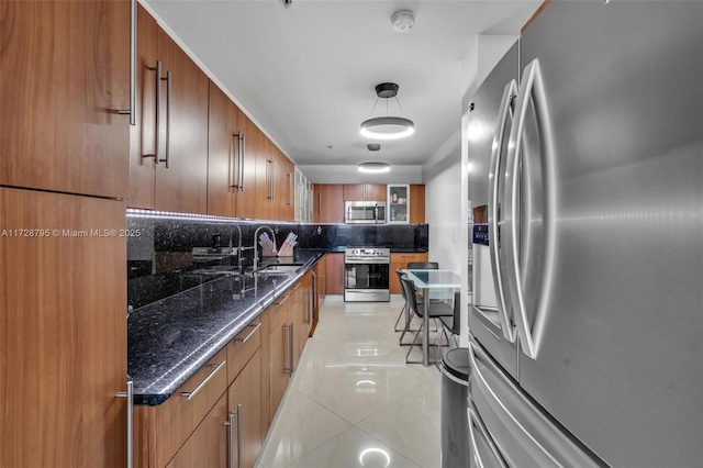 kitchen with pendant lighting, stainless steel appliances, dark stone counters, sink, and light tile patterned floors