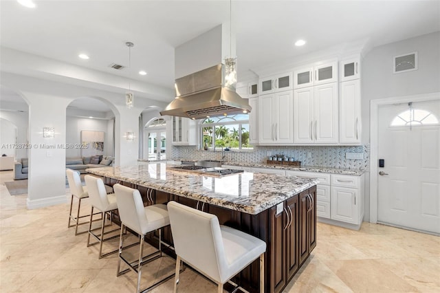 kitchen featuring light stone countertops, a spacious island, white cabinetry, hanging light fixtures, and island range hood