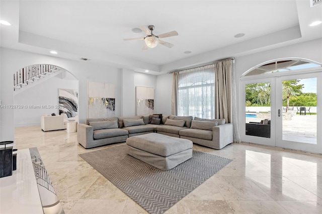 living room with a raised ceiling, french doors, and ceiling fan