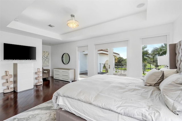 bedroom with access to exterior, dark hardwood / wood-style flooring, and a raised ceiling