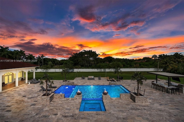 pool at dusk with a patio area, an in ground hot tub, an outdoor bar, a yard, and pool water feature